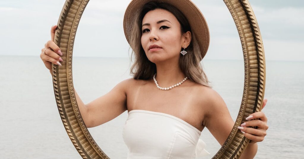 A woman in a white dress poses with a frame on a serene beach for an artistic portrait.