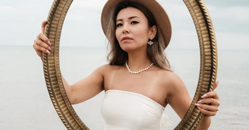 A woman in a white dress poses with a frame on a serene beach for an artistic portrait.